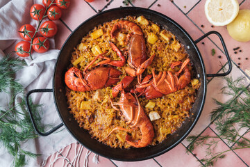 spanish seafood paella with lobster and squid, traditional dish with rice, top view of a hot pot, surrounded by fresh ingredients on a pink background table