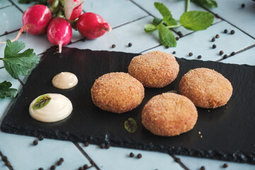 close up of delicious fried vegetable meatballs placed on black board and blue-tiled table, fresh ingredients and vegetables around