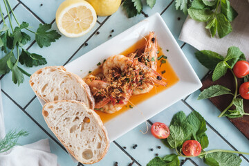 grilled prawns with fresh vegetables and white bread placed on a blue tiled table, fresh ingredients laying around, top view