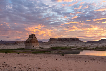 Panoramic view at sunset on solitary rock formations Lone Rock in Wahweap Bay in Lake Powell in Glen Canyon Recreation Area, Page, Utah, USA. Sand beach on wild campground. Red orange sky at sundown