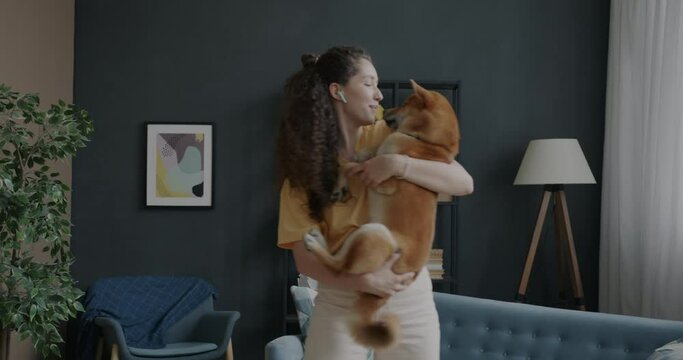 Cheerful girl dancing with pet dog singing having fun listening to music with earphones indoors in apartment. Leisure and entertainment concept.