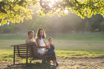 Cute family spending time in the park - sitting on a bench under the tree and looking in the camera