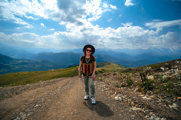 Front view. Tired woman in wide sun hat and backpack, tourist on hiking route to Koruldi Lakes, Svaneti region, Mestia Georgia. The concept of travel and active recreation. Summer day