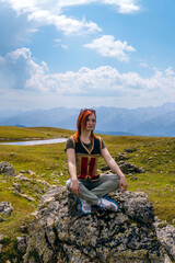 Naklejka premium Portrait of a young woman sitting in the lotus position on a rock boulder. Practices yoga. Vertical photo, Georgia. Summer day in the mountains of the Caucasus. Spiritual mood and relaxation