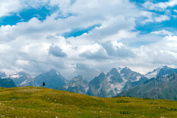 People, hikers walk far in the long distance, on a summer sunny day, against the background of snow-capped peaks of the Caucasus Mountains, Georgia