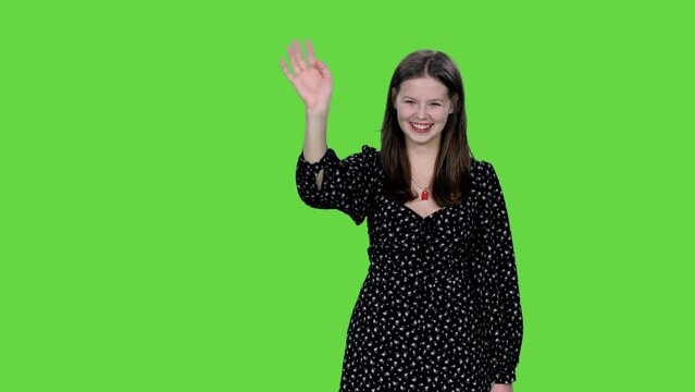 Smiling girl in polka dot dress waving hand hello on green background, Chroma key, 4k pre-keyed footage
