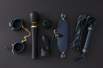 BDSM sex toys for role playing. Top view flat lay of leather handcuffs, mask, whip, vibrator massager, anal plug on black background