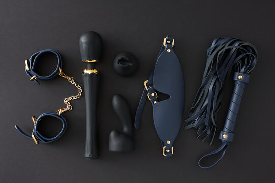 BDSM sex toys for role playing. Top view flat lay of leather handcuffs, mask, whip, vibrator massager, anal plug on black background