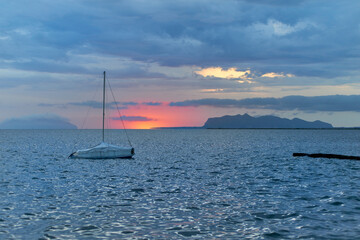 a sailboat moored at the Stagnone of Marsala in front of the Egadi islands at sunset and sky with dense blue clouds