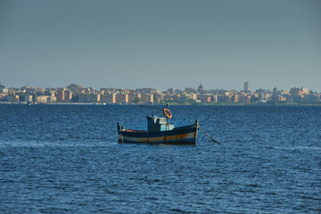 a typical wooden fishing boat with Marsala in the Province of Trapani in Sicily in the background