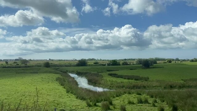Wide shot countryside & farmland farm clouds and blue sky out of a window of train, tracking along flat british UK southern England  - stock footage video