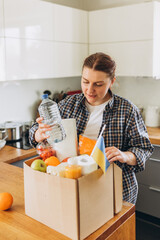 Female Volunteer holding box with groceries and flag of Ukraine on the house kitchen background. Donation box with food in female hands. Concept of humanitarian, donations or helping