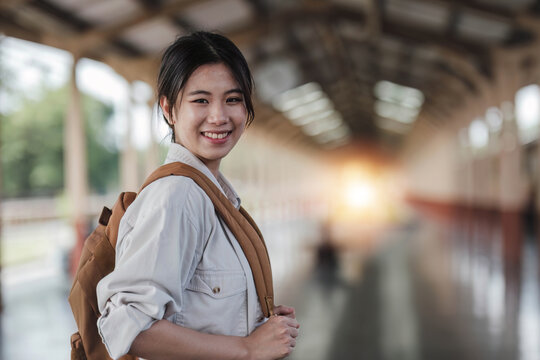 Asian backpack traveler woman with camera standing at train station platform and waiting train arrivel, summer holiday travelling or young tourist concept