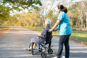 Caregiver help and care Asian elderly woman on wheelchair at park with happy in holiday.
