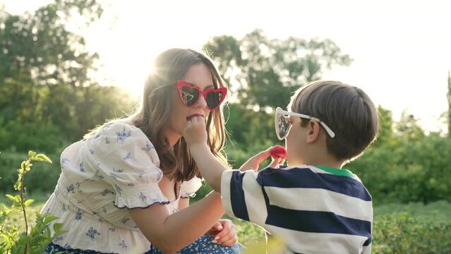 Cute little boy and mother feeding each other red strawberries at home garden
