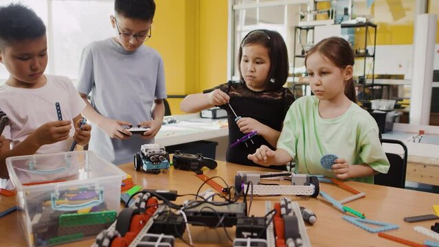 Children at the table in a class at a robotics lesson assemble modules for moving robots with hands and screwdrivers and check how it works with a joystick. Concept of technological modern education