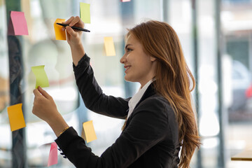 Happy businesswoman planning ideas project work on a glass of wall with colorful memo