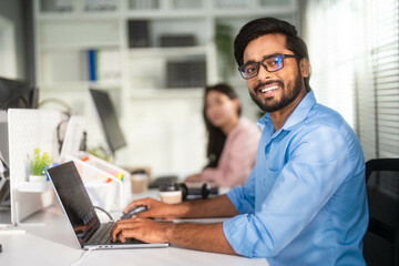 Obraz premium Portrait of Indian man which smiling while working with laptop at the office and looking at camera.