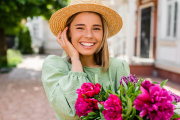 beautiful young woman in summer style outfit smiling happy walking with flowers in city street