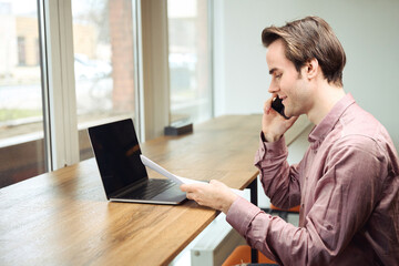 Joyous worker dealing with business documentation during phone conversation