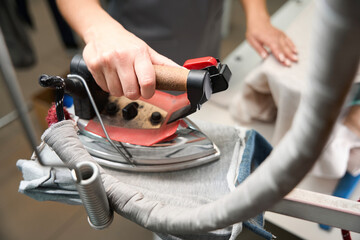 Woman laundry office operator taking hot iron with steam to remove wrinkles