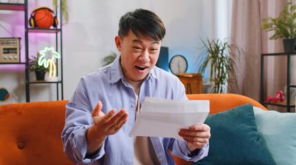 Asian man open envelope letter, reading it. Career growth advance promotion, bank loan approve, successful admission to university monetary award long-awaited invitation great news, lottery game win