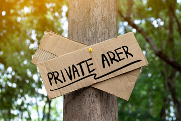 Private Area on paper signpost sticked on tree in the public park to warn people to avoid walking or entering into this area and not arrow to stay in this area, soft and selective focus.