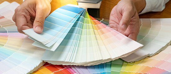 Designer hand choosing color swatch samples catalog or rainbow colour palette guide for selection...