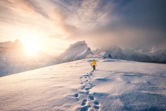 Mountaineer walking with footprint in snow storm and sunrise over snowy mountain in Senja Island