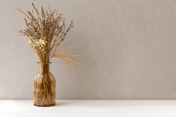 Minimalistic composition of dried flowers in glass brown vase on gray vintage textured wall...