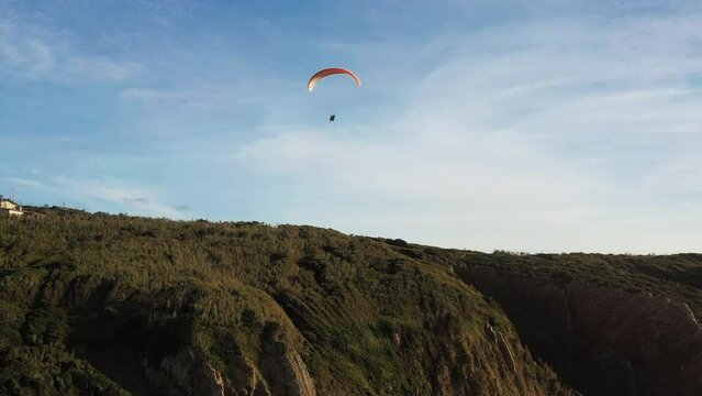 Extreme paraglider flying in clear blue skies, toward cinematic teal ocean. Unrecognizable person flies with paraglide near Atlantic ocean