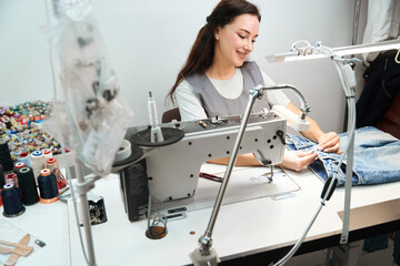 Woman tailor sewing button back on denim pants after dry cleaning process