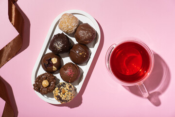 Chocolate craft nuts candies on pink background with cup of tea top view, flat lay.