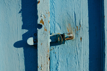 Close-up of an old slightly rusty door handle on a wooden textured door with shabby faded blue...