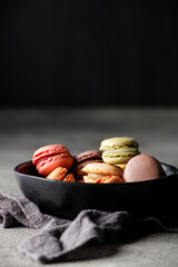 Different macaroons in a black bowl on a towel. Black background, close-up, free space for text