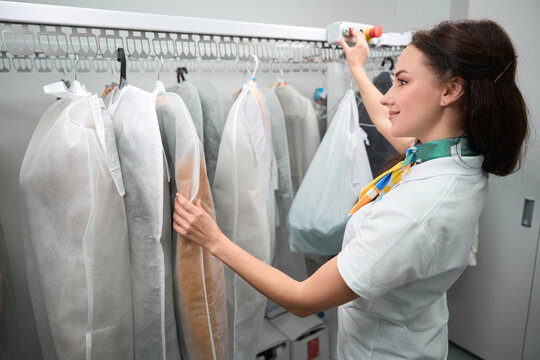 Smiling laundry office worker pushing button to rotate rack with clothes