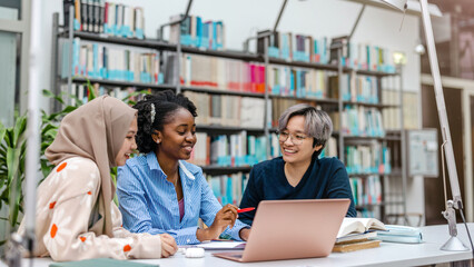 Multiethnic group of students sitting in a library and studying together
- 613581599