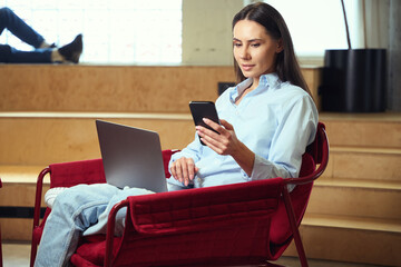 Concentrated female freelancer reading something on her mobile phone indoors
