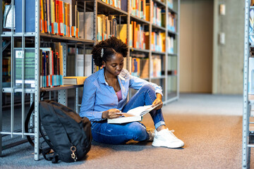 Black female student reading a book in a library
