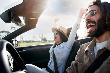 Young excited heterosexual caucasian couple driving a car. They are in vacation trip happy under...