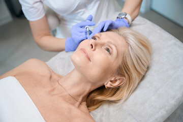 Obraz na płótnie Canvas Happy adult lady getting cheekbone injection in beauty salon