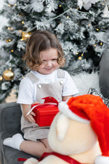 Portrait of a cute little girl near decorated Christmas and new year tree at home. Smiling, cheerful and happy, holding red gift box. Festive cozy home atmosphere, family time