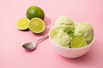 Ice cream with lime flavor and slices of fresh lime in a white bowl, pink background, copy space. Summer cooling desserts,