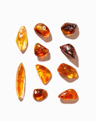Set of Natural gemstone amber stones with glare shadows, yellow orange isolated on white background. Natural mineral Transparent amber gems different forms, flat lay pattern, minimal top view