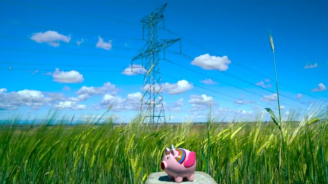 Una persona echando monedas en una hucha de cerdito unicornio en un campo de trigo con torres el&eacute;ctricas a su espalda como concepto del precio de la electricidad, ahorro energ&eacute;tico, medioambiente, etc