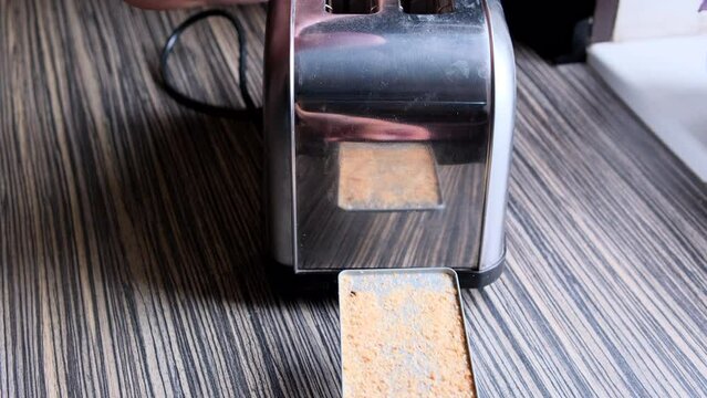 Close of a man's hands sliding out a full tray of dry bread crumbs from the bottom of a traditional chrome toaster, then emptying the tray and putting it back in place.