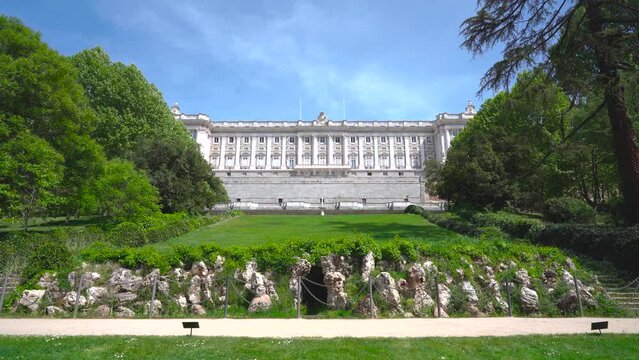 View of the Royal Palace of Madrid and the secret door from the gardens on a sunny day with wind and moving vegetation, from the city of Madrid, Spain.