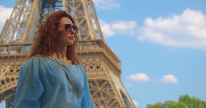 Smiling tourist woman looking at landmark on a famous Eiffel Tower. Woman on vacation in the french capital city, walking around the Eiffel tower. Eiffel Tower is most photographed landmark
