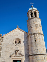 Fototapeta na wymiar Facade with a rose window and tower of the Church of Our Lady of the Rocks. It is in an artificial island in the Adriatic sea. Perast, Kotor Bay, Montenegro