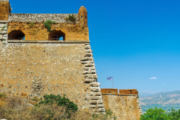 Nafplio, Greece Palamidi fortress bastions Miltiadis and Leonidas with a Greek flag waving against a blue sky. - obrazy, fototapety, plakaty